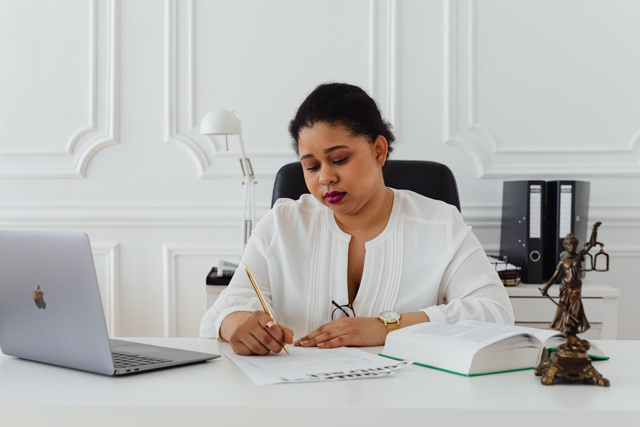 African American woman lawyer signing documents at a desk, symbolizing professionalism.