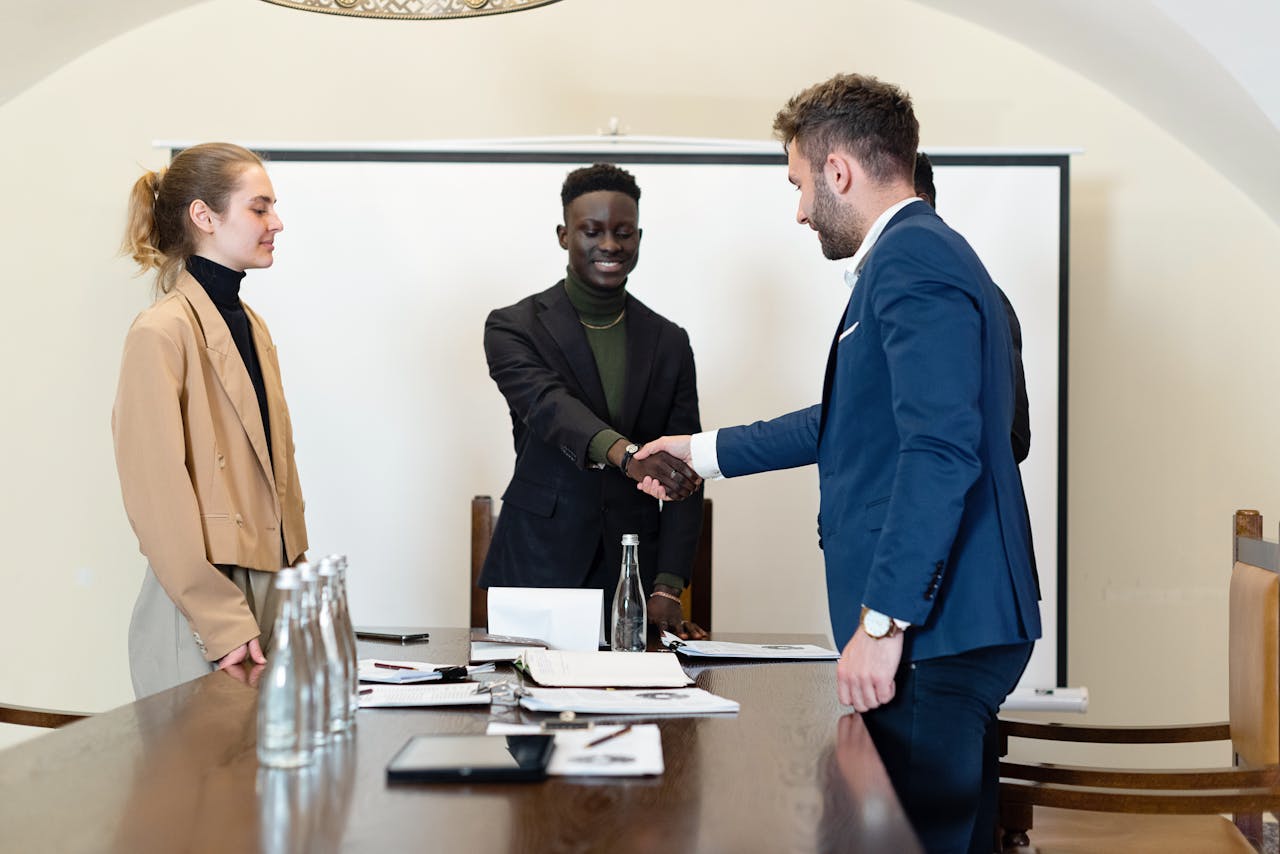 A diverse group of business professionals in a meeting room, shaking hands as a sign of agreement.